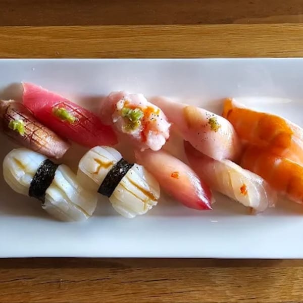 A white rectangular plate holds various pieces of colorful sushi and sashimi, including tuna, squid, and salmon.