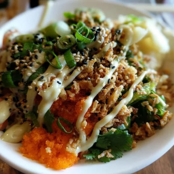 Close-up of a Toro Sushi Poke House poke bowl with roe, fried onions, green onions, and sauce.