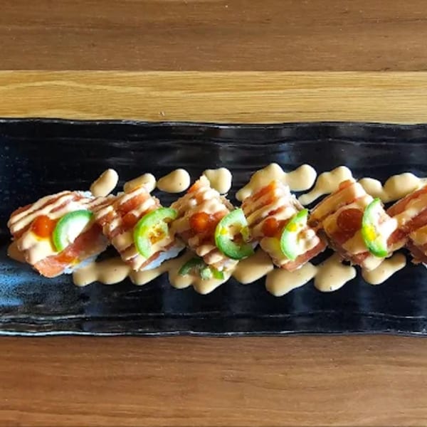 Toro Sushi Poke House's salmon sushi with avocado, jalapeño, and spicy mayo on a black plate.