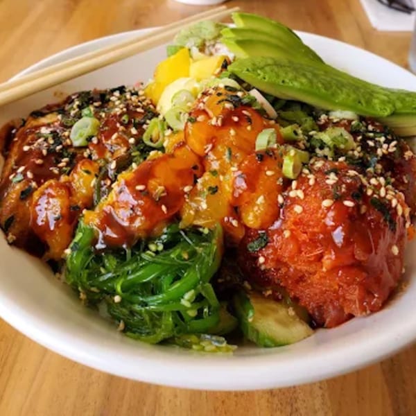 A colorful poke bowl with tuna, salmon, avocado, seaweed salad, and mango, garnished with sesame seeds.